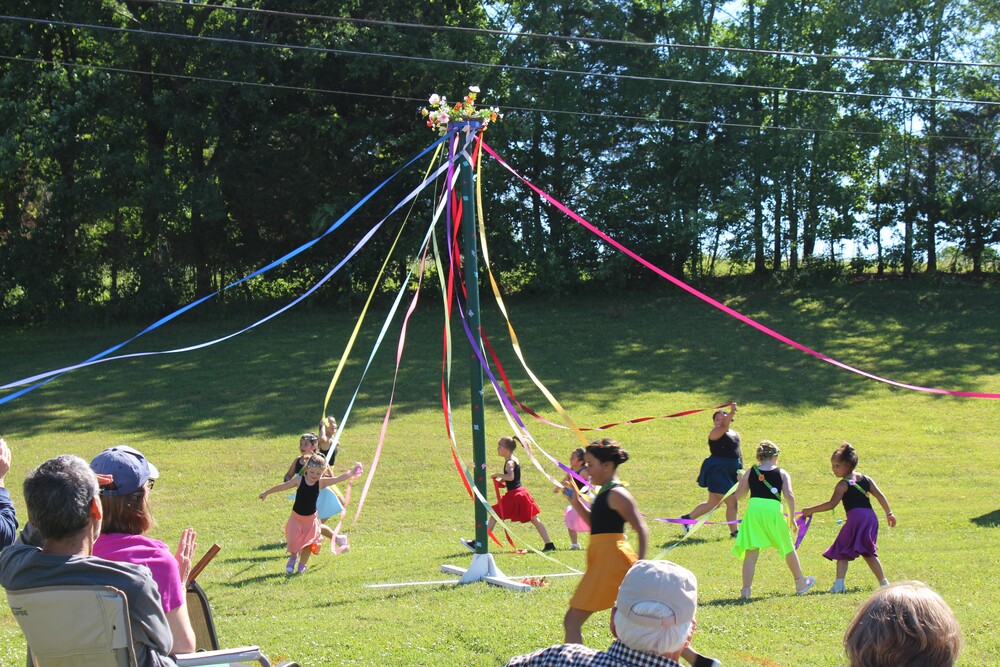 Children dance around the may pole carrying ribbons